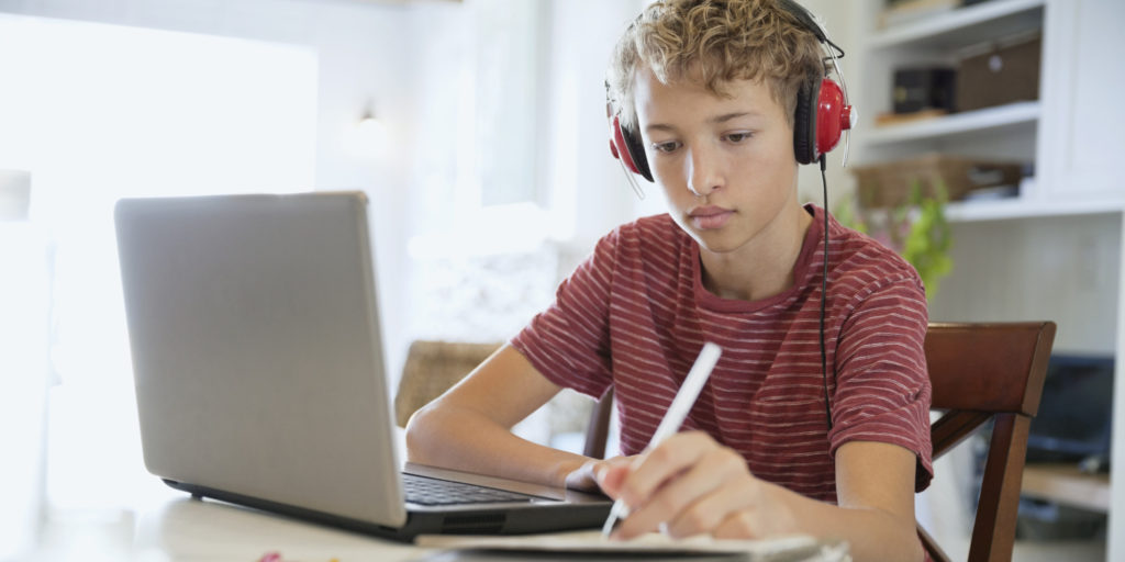 brainfood boy making notes on writing pad while using laptop and headphones   
